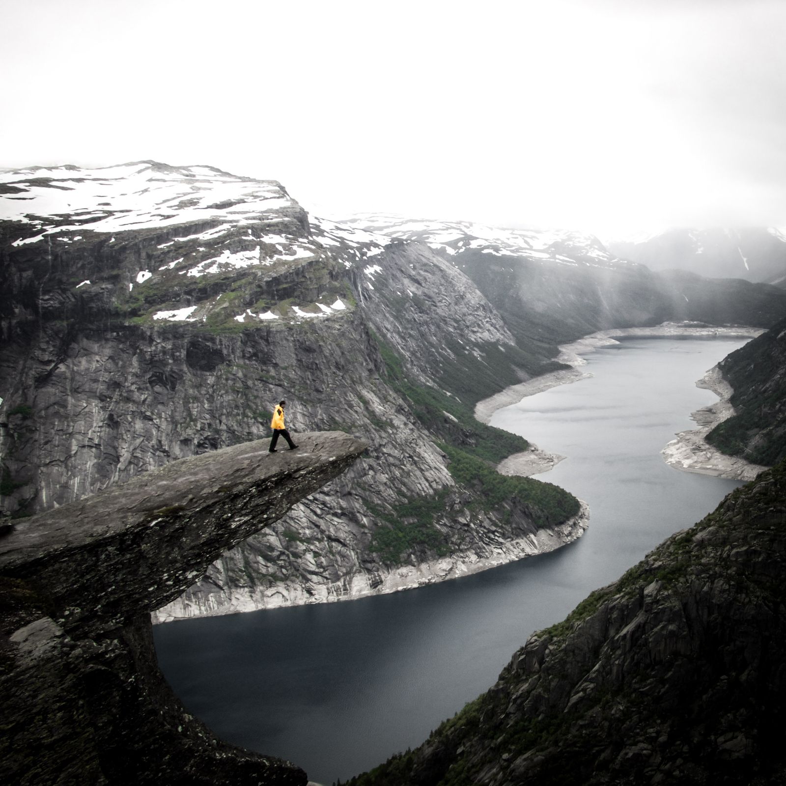 Person standing on a cliff ledge above a fjord