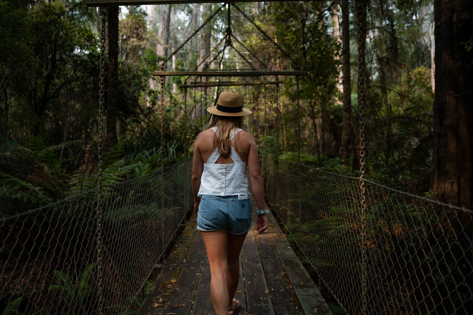 Woman walking across a wooden suspension bridge through a forest