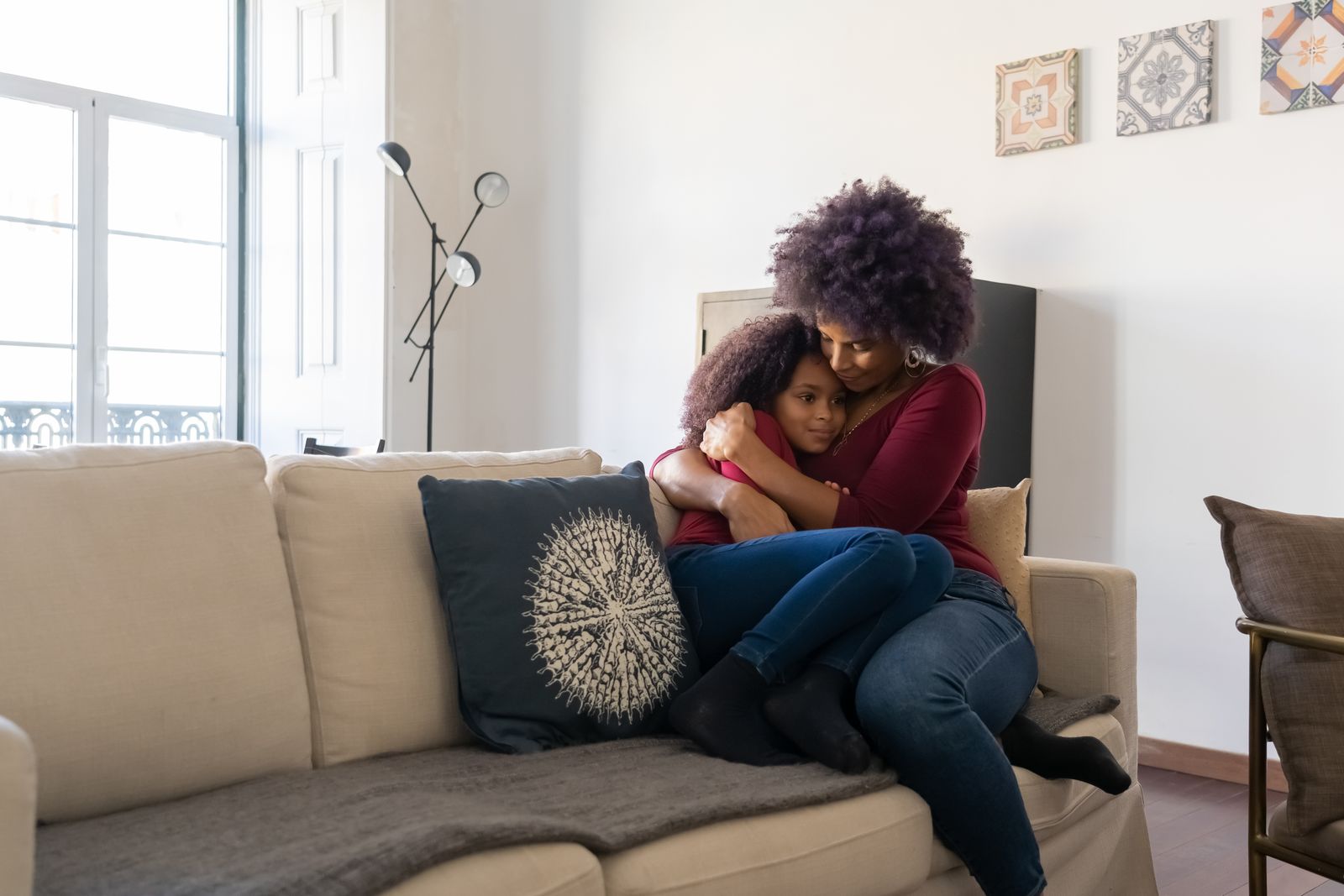 Mother hugging her daughter closely on a sofa in a bright living room