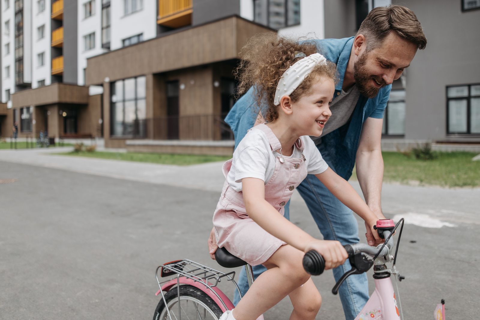 Father steadying his smiling daughter as she learns to ride a bike